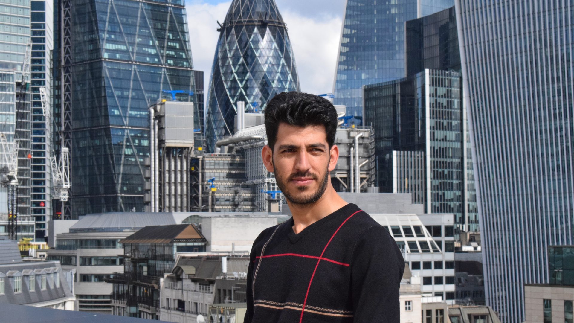Young man in black jumper stood in front of City of London skyline