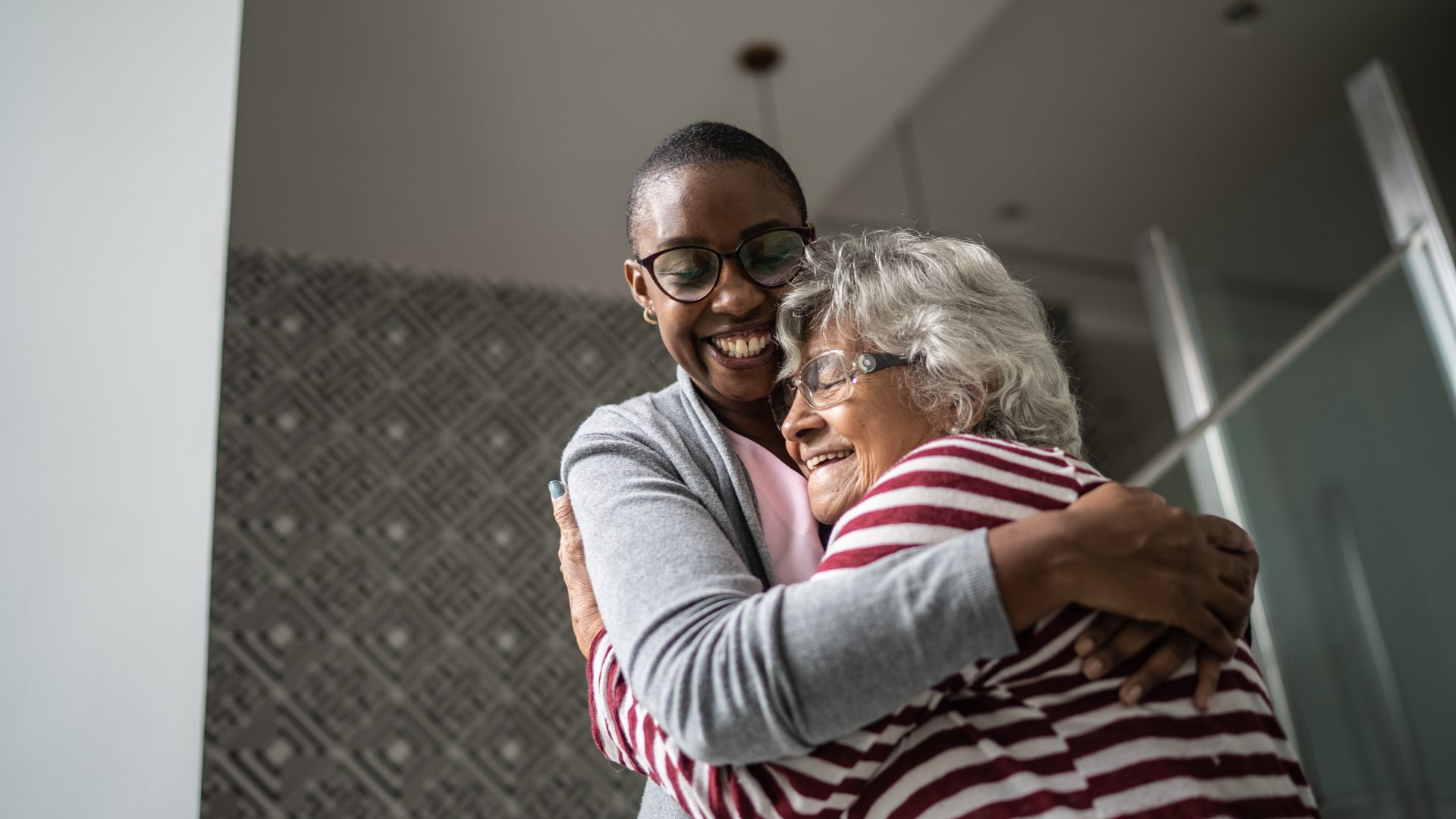 A younger carer and older lady hugging and smiling in home environment