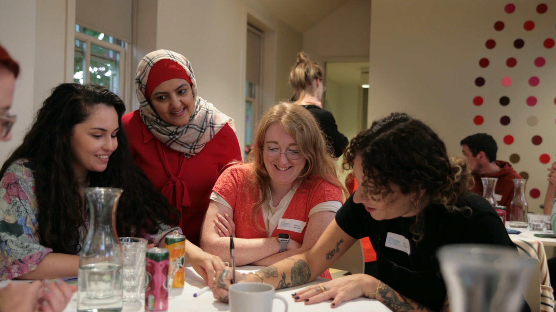 A group of smiling people sat around a table, writing answers on a piece of paper.